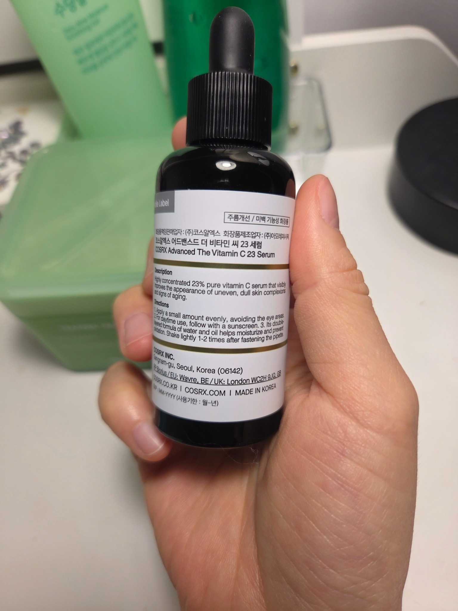 Back label of COSRX The Vitamin C 23 Serum bottle held in hand, showing product information text