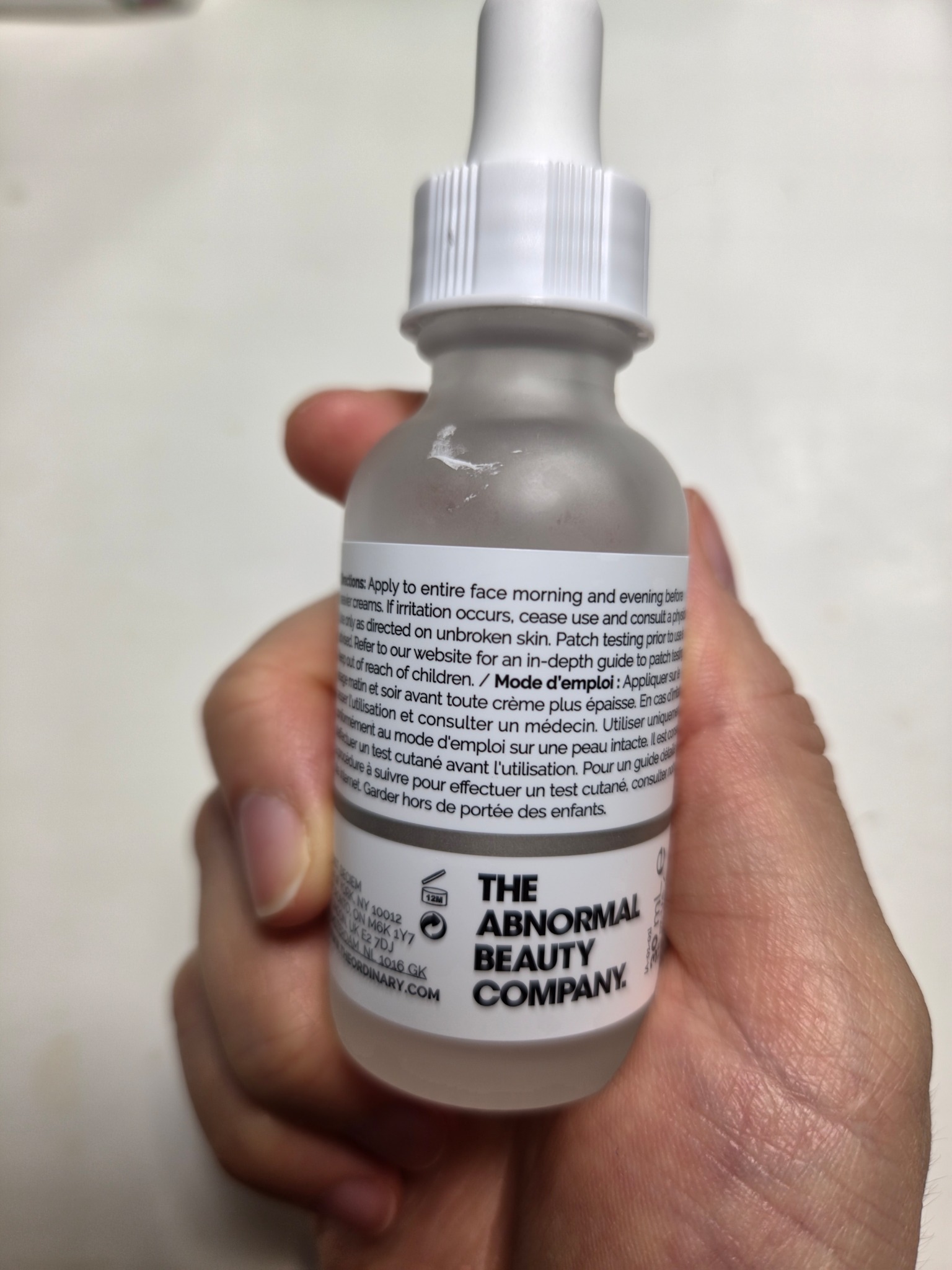 Back label of The Ordinary Niacinamide 10% + Zinc 1% bottle held in hand, showing directions and product details